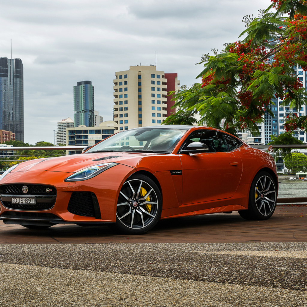 Оранжевый автомобиль Jaguar F-Type на фоне небоскребов 