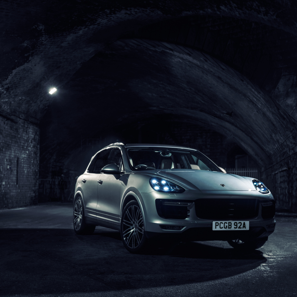 Серебристый автомобиль Porsche Cayenne в тоннеле с включенными фарами