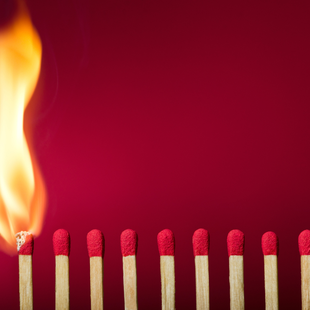 Зажженная спичка и спички на красном фоне