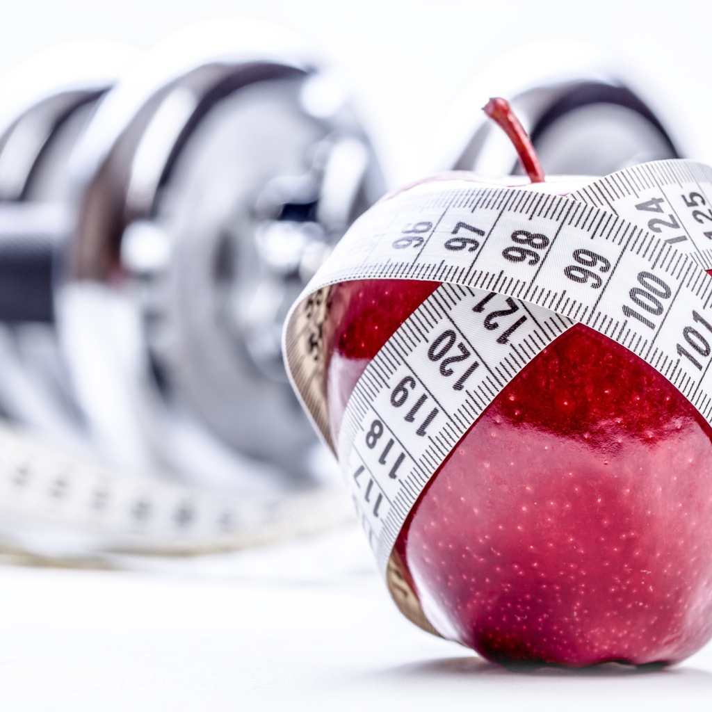 Красное яблоко перемотано мерной лентой и гантели на белом фоне