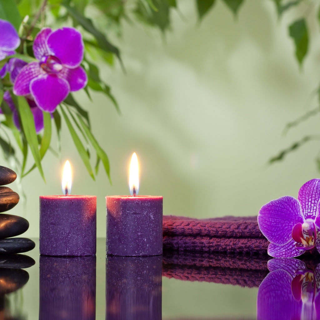 Две горящие свечи с камнями и цветами орхидеи отражаются в зеркальной поверхности стола