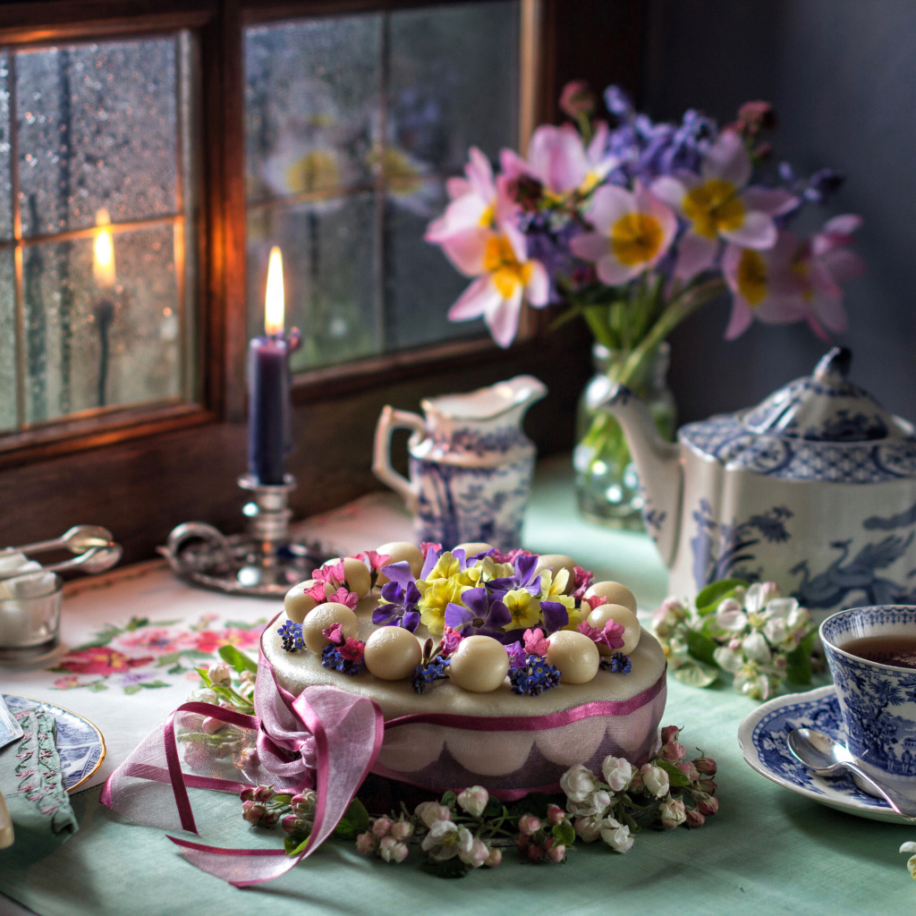 Красивый торт на столе с сервизом и горящей свечой у окна