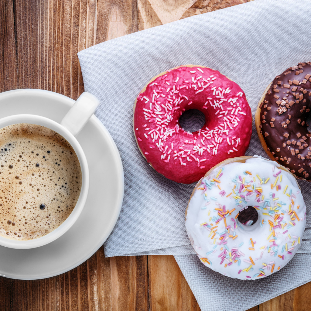 Чашка кофе с тремя аппетитными пончиками на столе