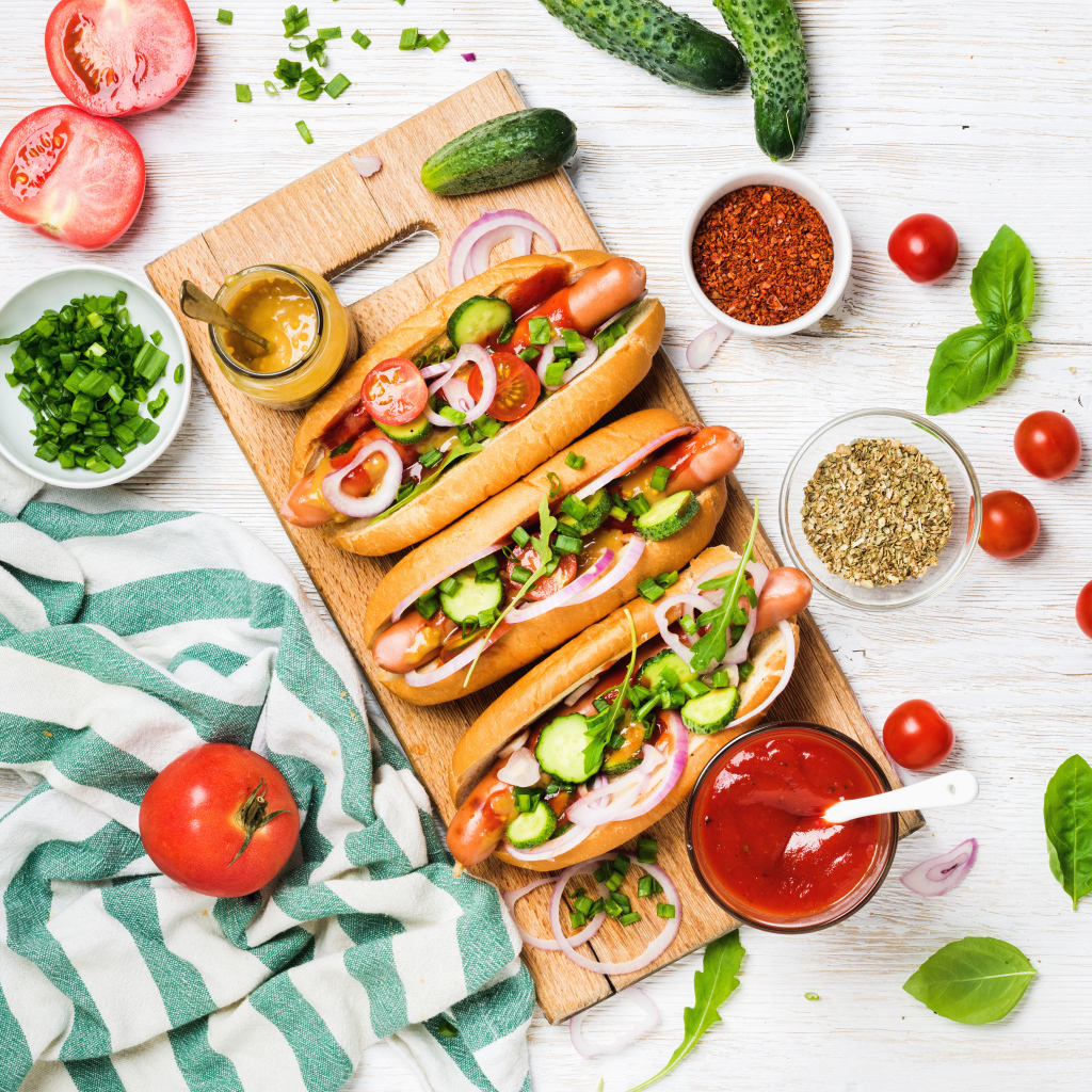 Аппетитные хотдоги на разделочной доске с овощами