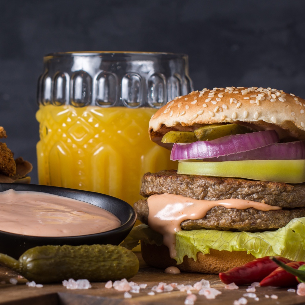 Аппетитный гамбургер на столе с соусом, овощами и соком