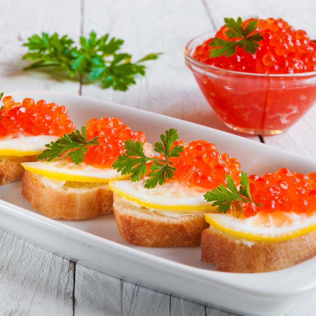 Бутырброды с красной икрой и лимонами на белой тарелке