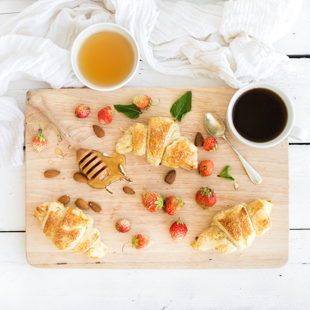 Круассаны, мед, свежие ягоды клубники и кофе на завтрак