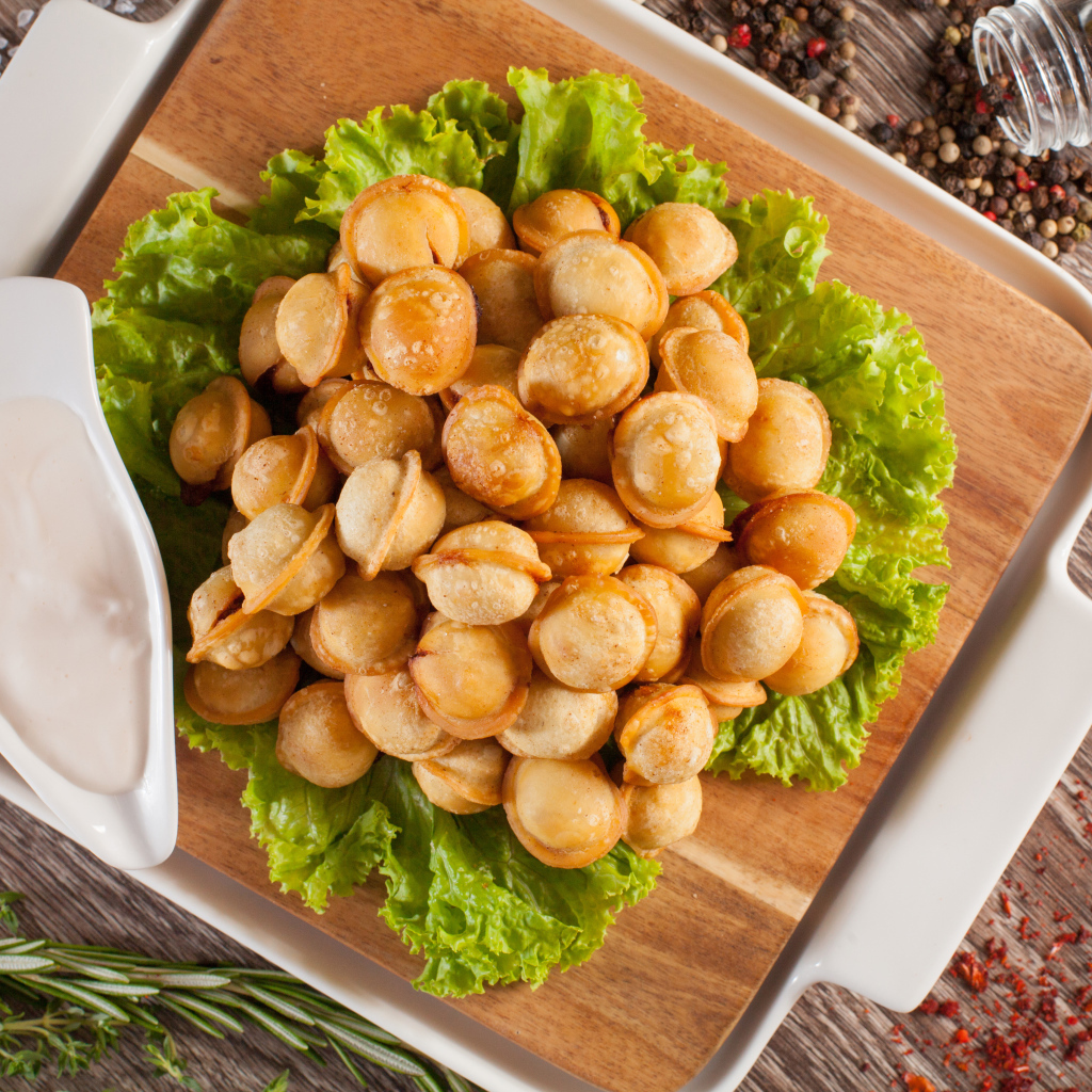 Пельмени с соусом и листьями салата лежат на разделочной доске