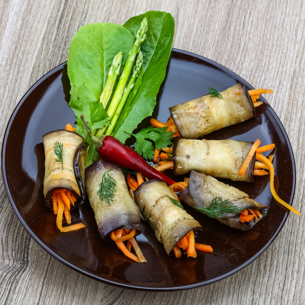 Рулетики из баклажанов с морковью на тарелке с листьями салата