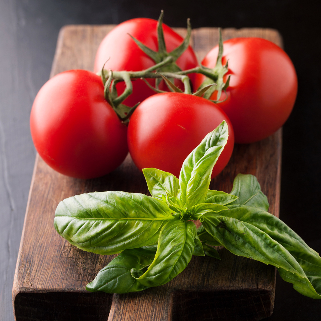 Свежие помидоры на разделочной с зеленью