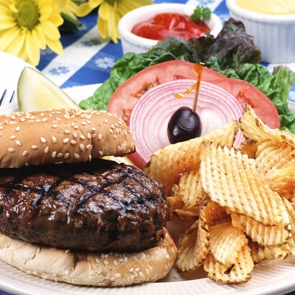 Гамбургер с котлетой и картофельные чипсы на тарелке с овощами