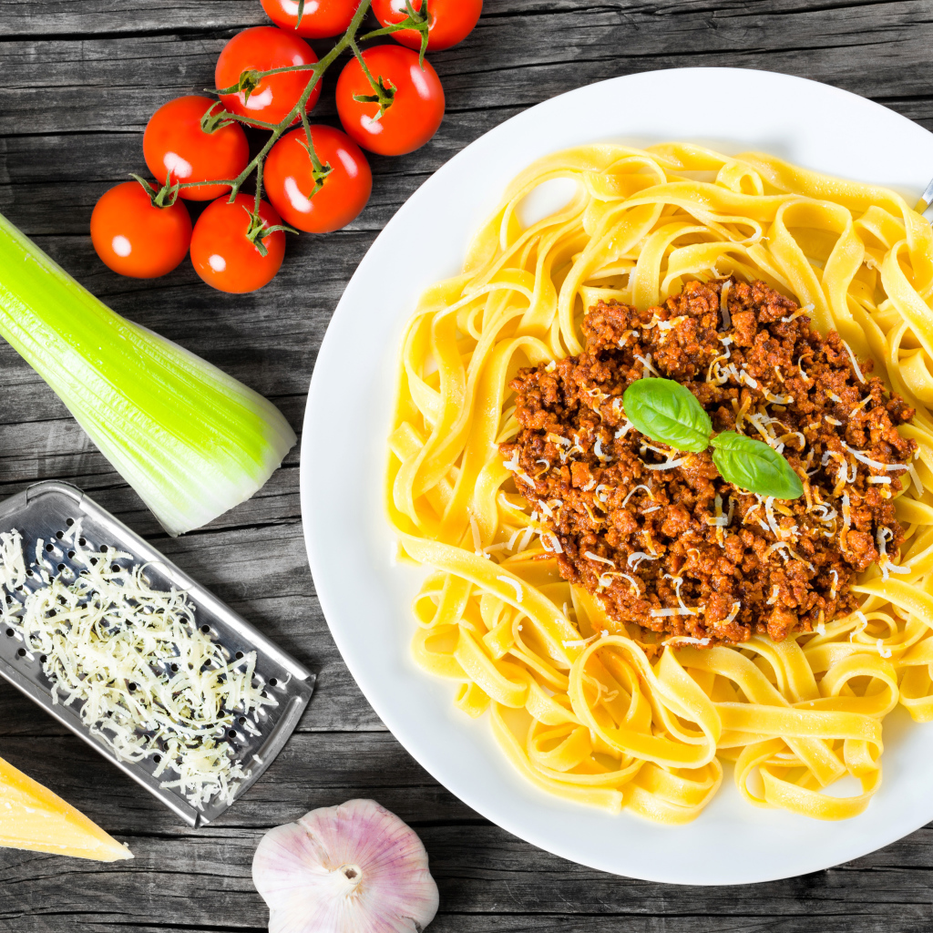 Спагетти на белой тарелке с мясом и сыром
