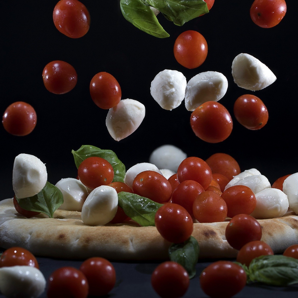 Помидоры и сыр Моцарелла падают на пиццу 