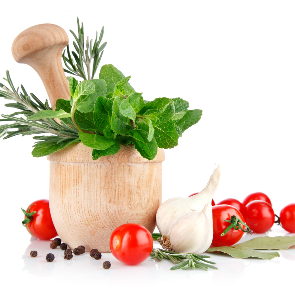 Деревянная ступа и пестик со специями и зеленью на столе с чесноком и помидорами