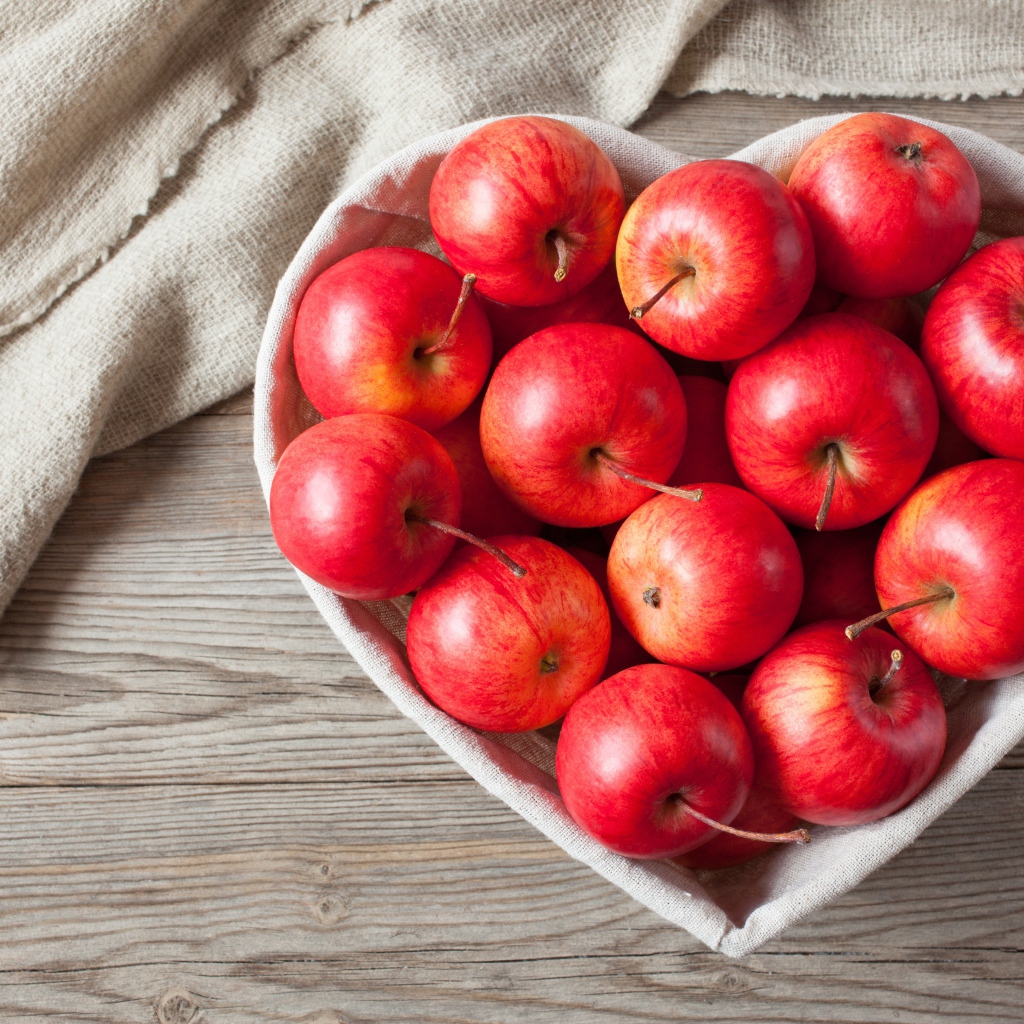 Красивые красные яблоки в тарелке в форме сердца на столе