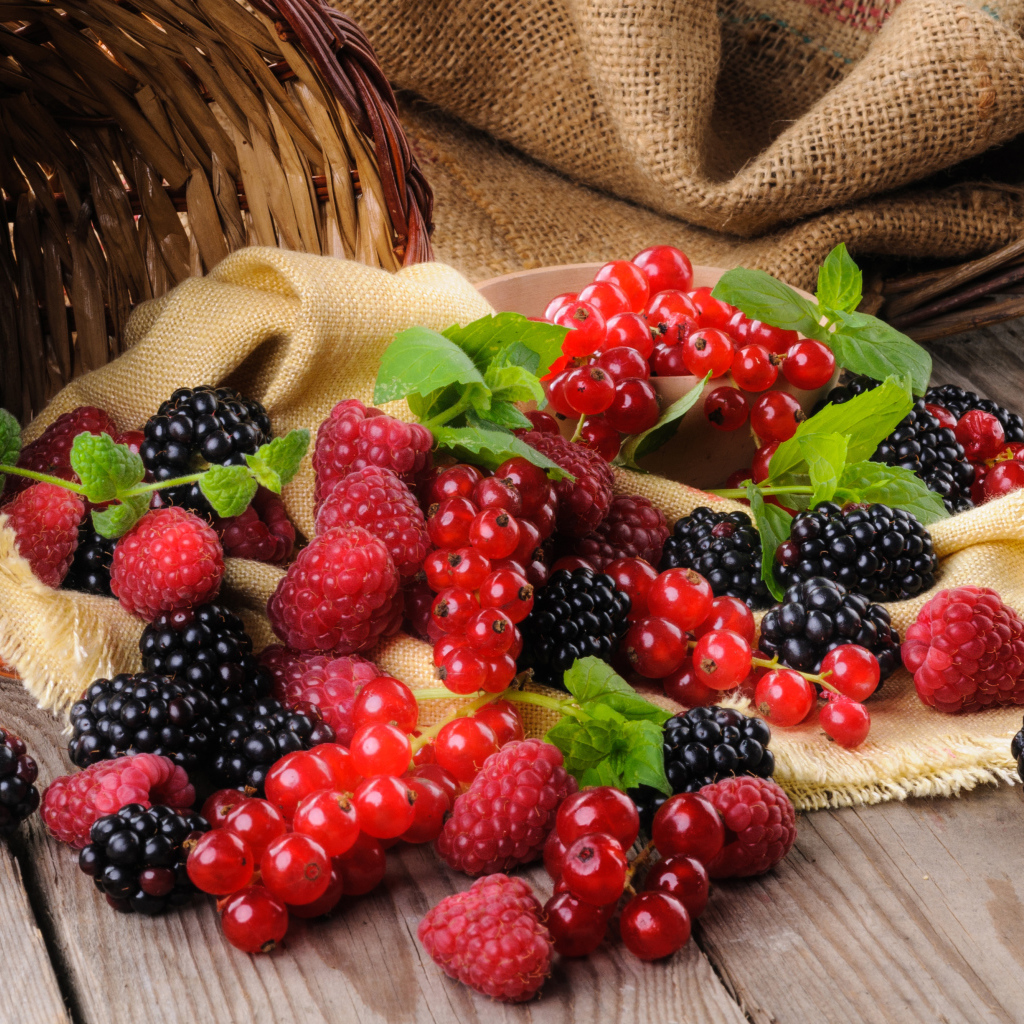 Свежие ягоды ежевики, малины и красной смородины с корзиной на столе