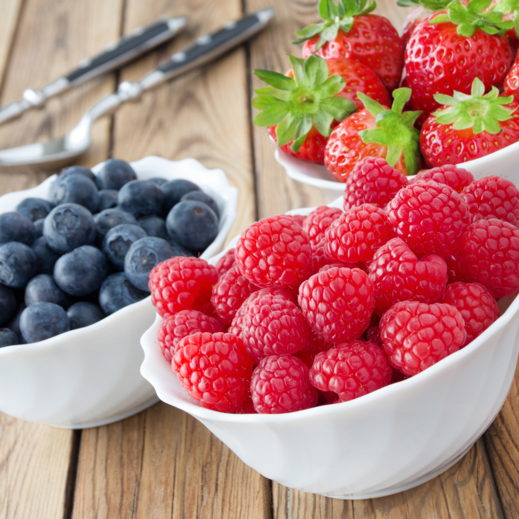 Свежие ягоды малины, клубники и черники в белых тарелках на столе