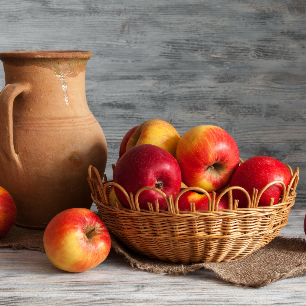 Красные яблоки в корзинке на столе с кувшином