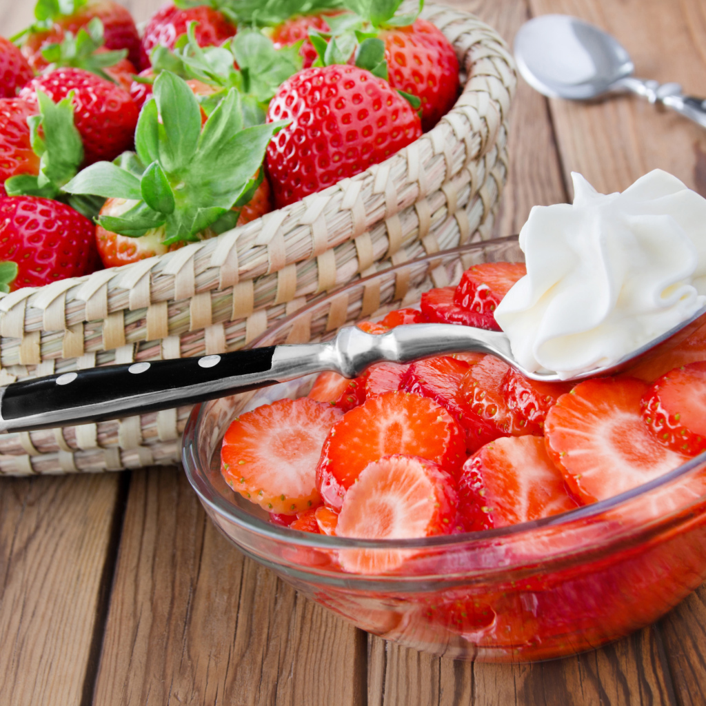 Нарезанная клубника в стеклянной посуде с ложкой сливок