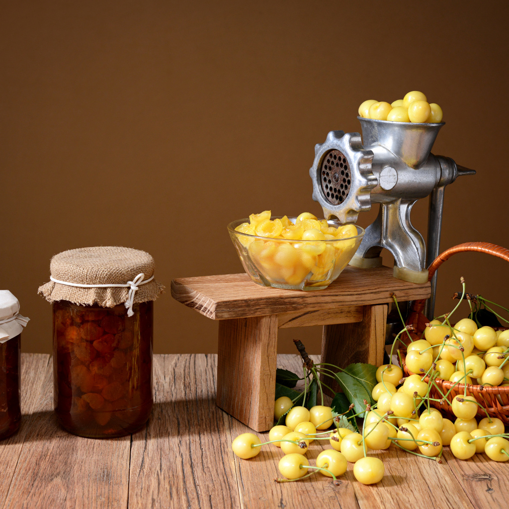 Две баночки варенья и желтые черешни на столе с мясорубкой