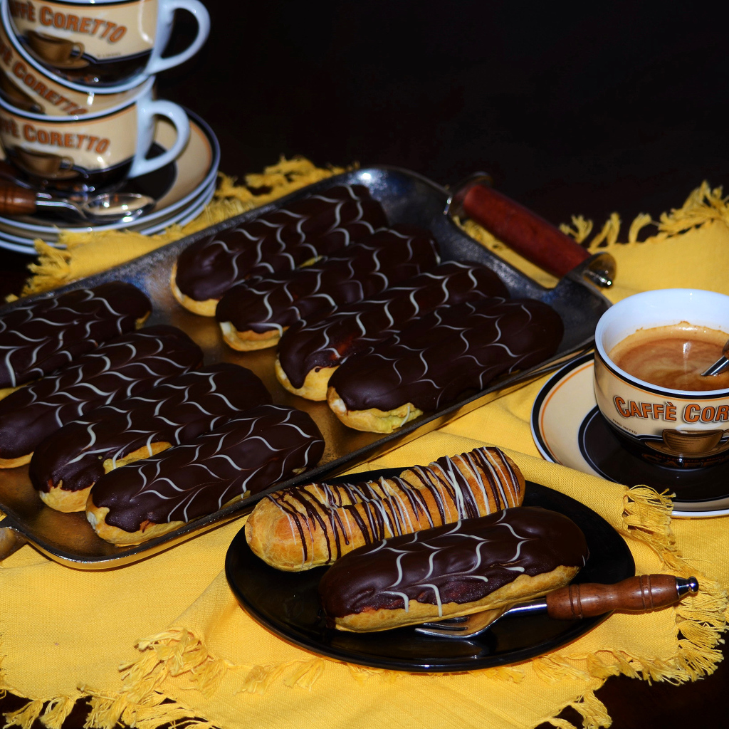 Аппетитные сладкие эклеры с шоколадом и чашками кофе на столе