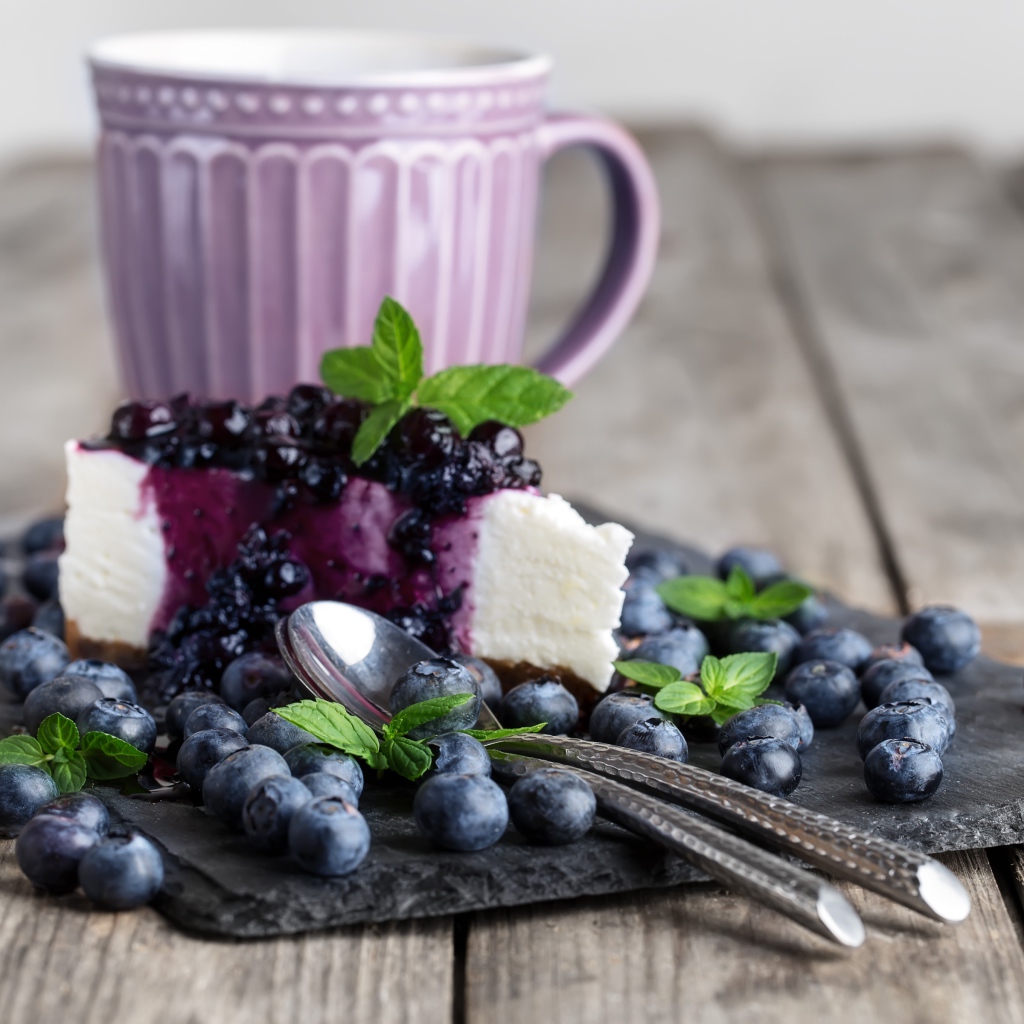 Черничный чизкейк со свежими ягодами лежит на столе с чашкой