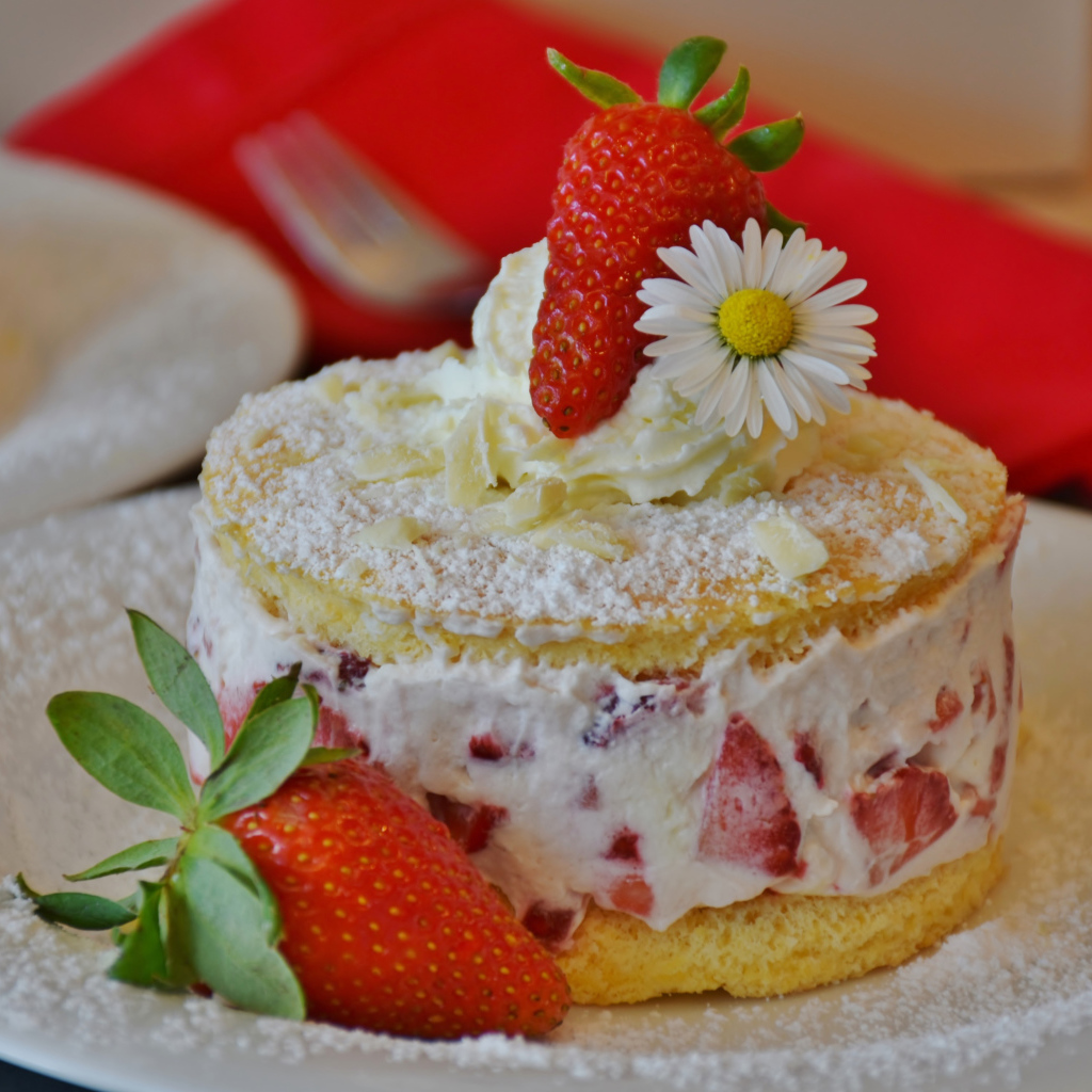Торт со сливочным кремом и свежими ягодами клубники на белой тарелке