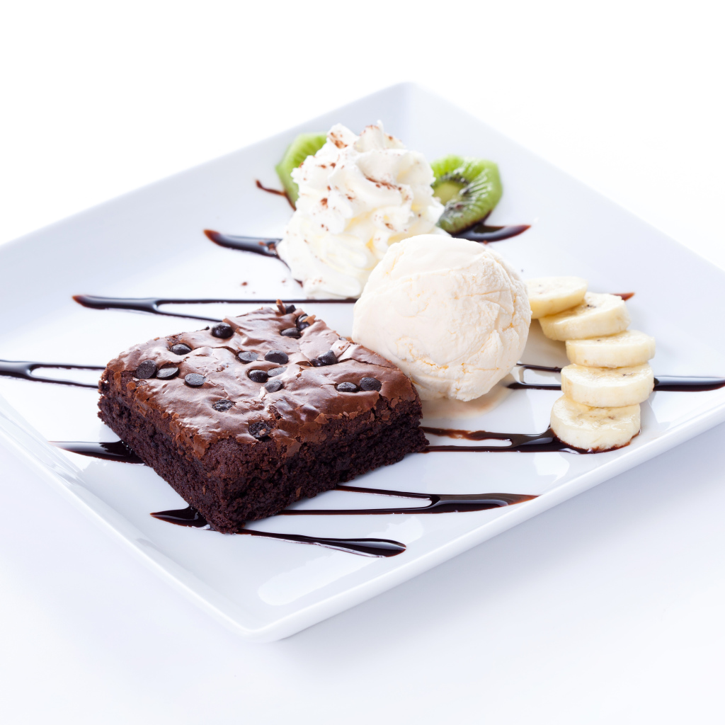 Шоколадное пирожное с мороженым, сливками и кусочками банана на белой тарелке