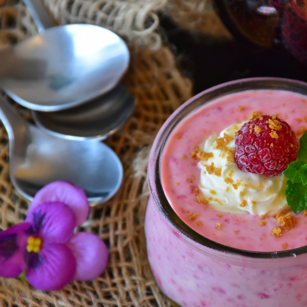 Десерт с малиной и кремом на столе с ложками