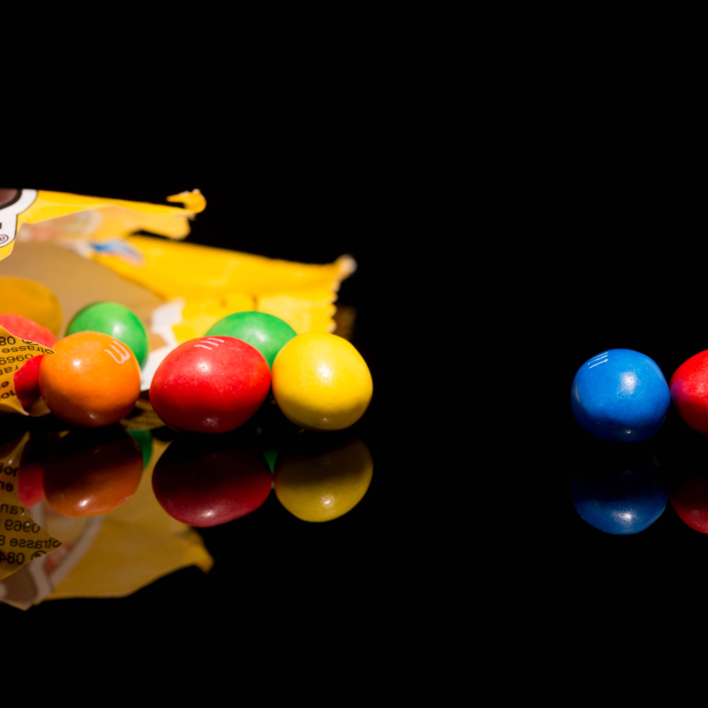 Разноцветные конфеты  M&m's отражаются в черной поверхности стола 