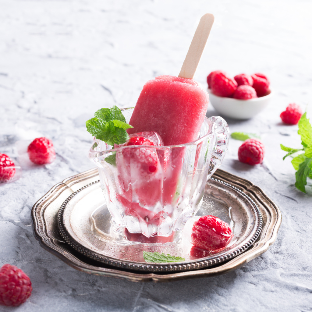 Малиновое мороженое на палочке в стеклянном стакане на столе со свежими ягодами