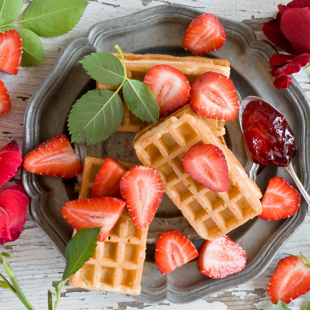 Сладкие вафли со свежей клубникой и красными розами на столе