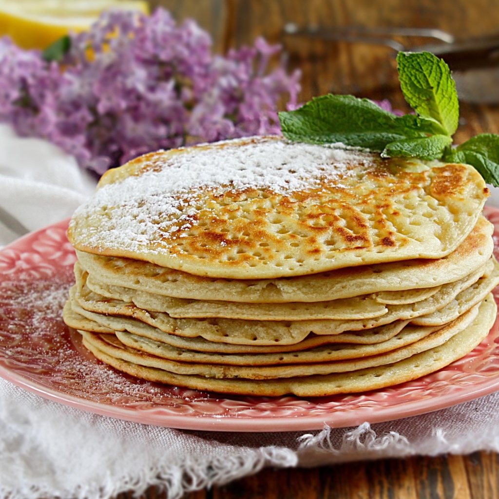 Тонкие блинчики на тарелке с сахарной пудрой и веточкой мяты