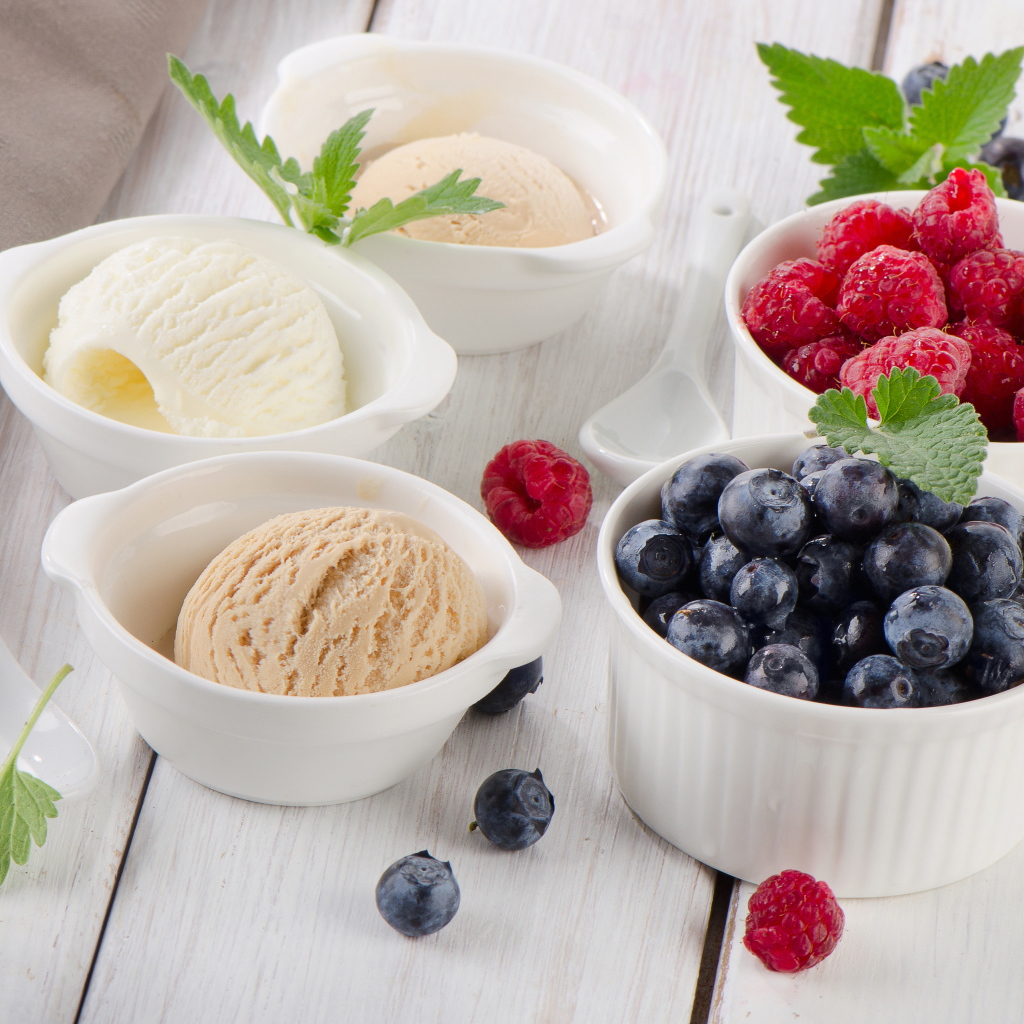 Три шарика мороженого и свежие ягоды малины и черники в белых тарелках