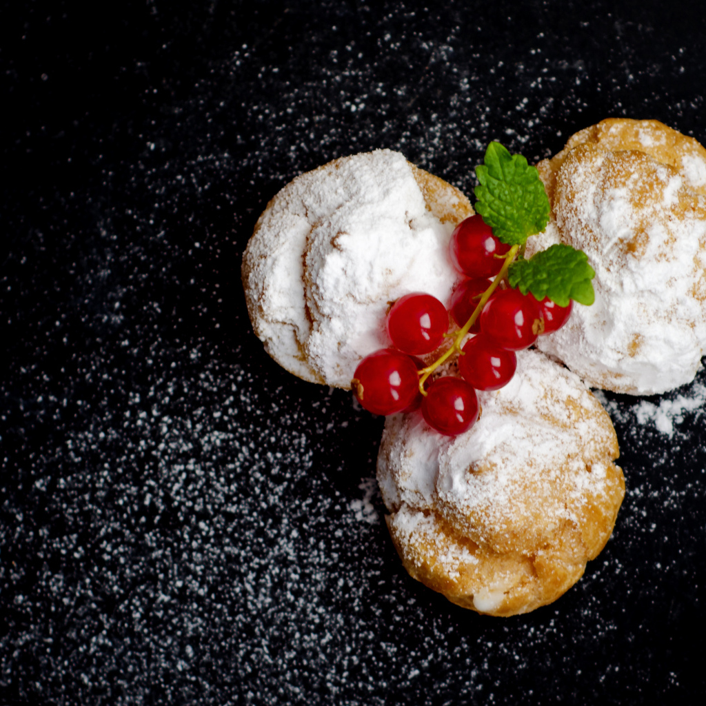 Три пирожных с сахарной пудрой и красной смородиной на черном фоне