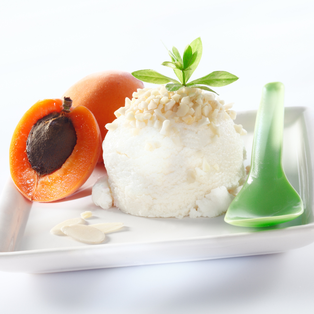 Шарик ванильного мороженого с абрикосами на белой тарелке с ложкой