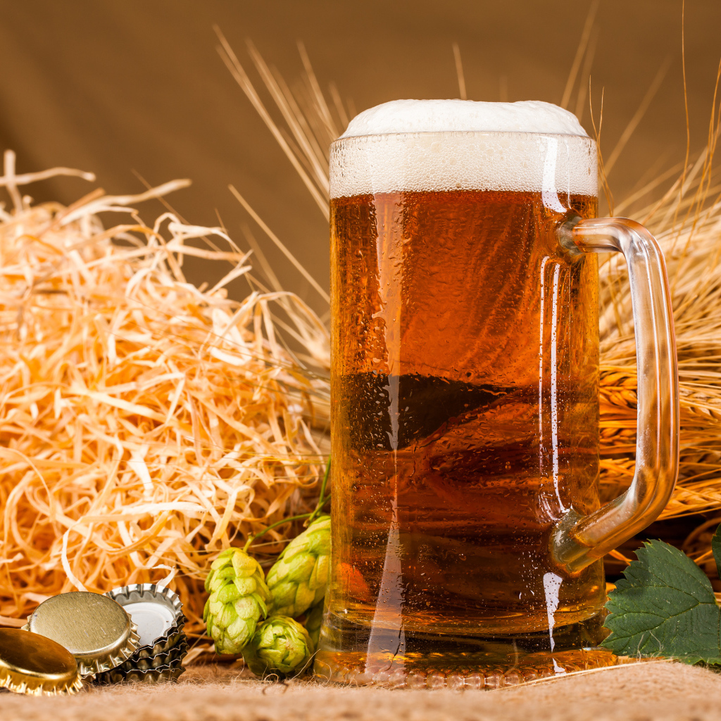 Бокал пива с пеной на столе с хмелем и соломой