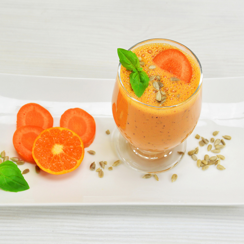 Бокал морковного коктейля с апельсином на белой тарелке