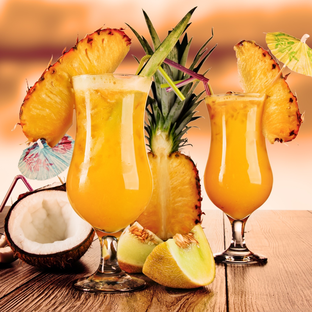 Тропические коктейли на столе со свежими ананасом, кокосом и кусочками дыни