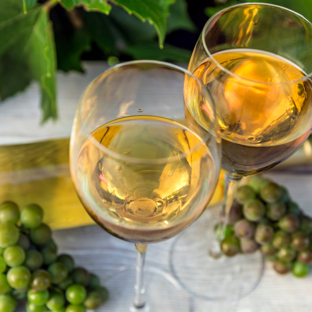 Два бокала белого вина с белым виноградом на столе