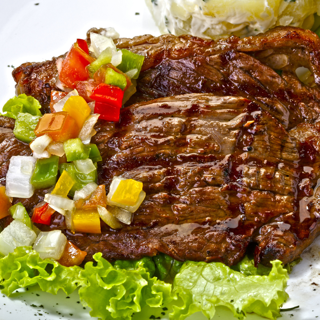 Кусок сочного жареного мяса с овощами и листьями салата