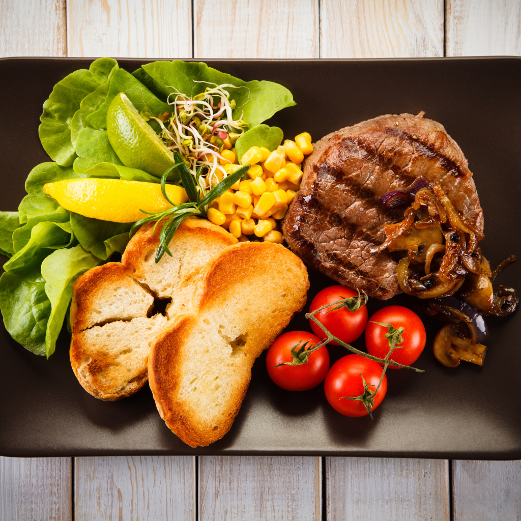 Аппетитный кусок жареного мяса на тарелке с овощами и гренками