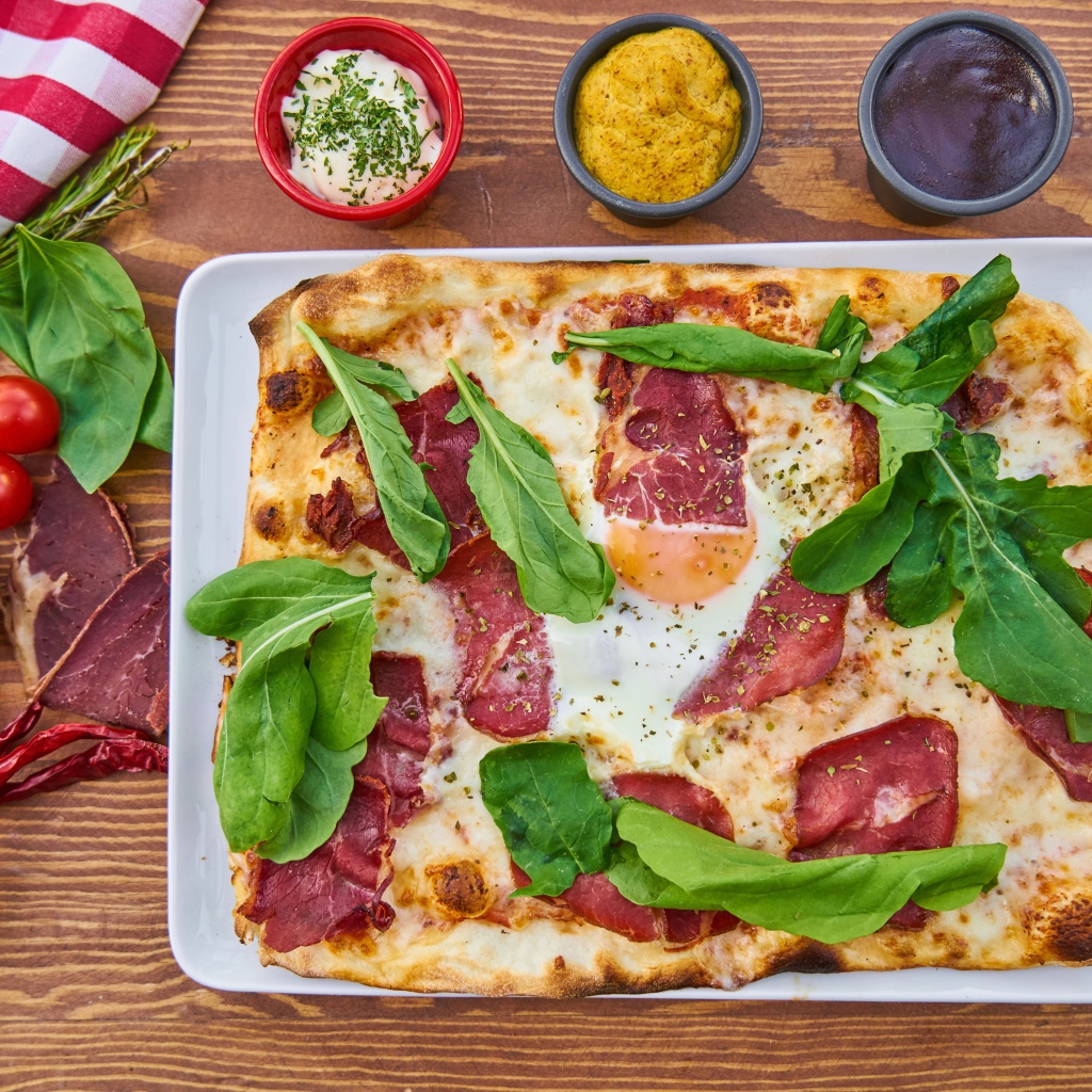 Пицца с беконом и зелеными листьями базилика на столе 