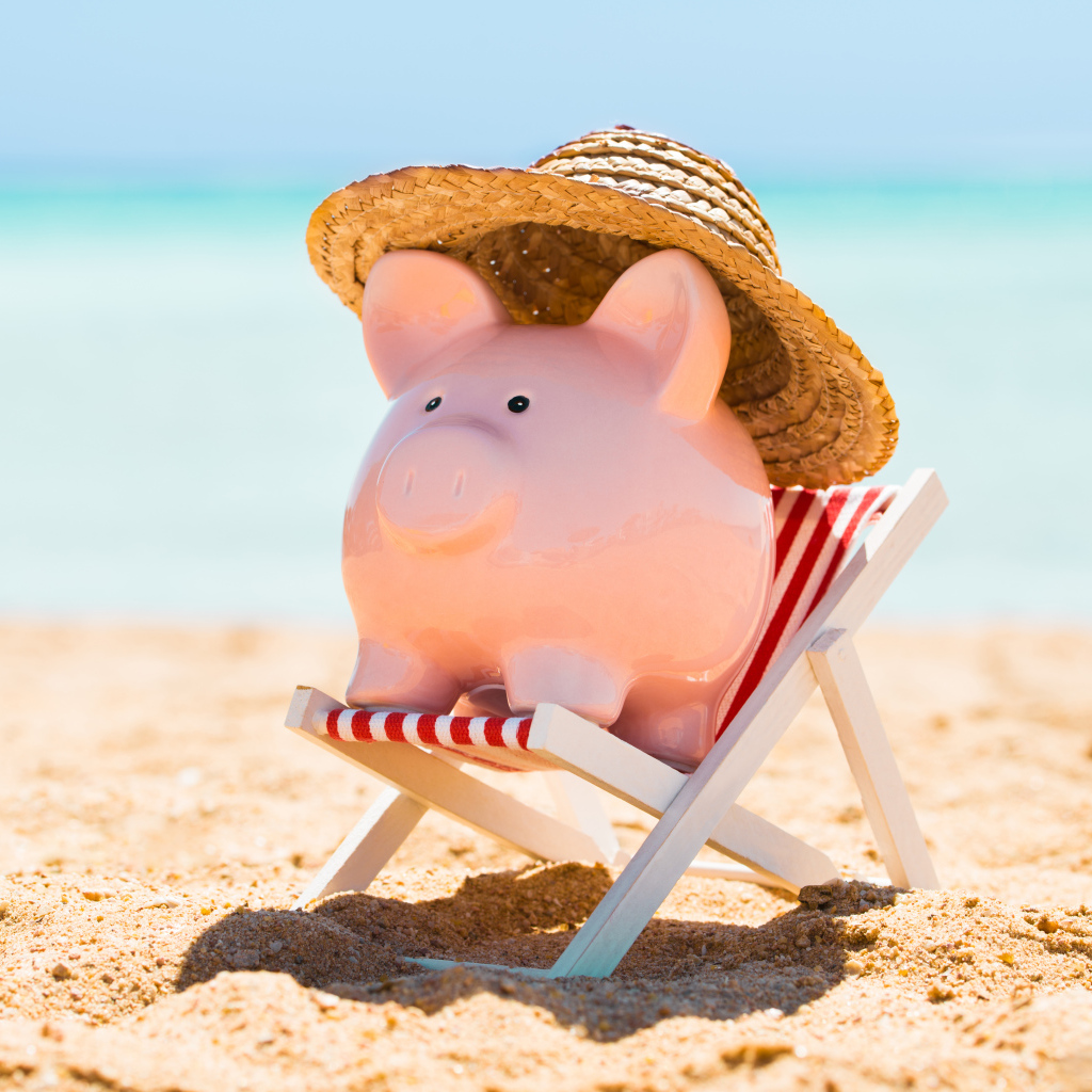 Сувенир свинка в шляпе лежит в игрушечном кресле на пляже