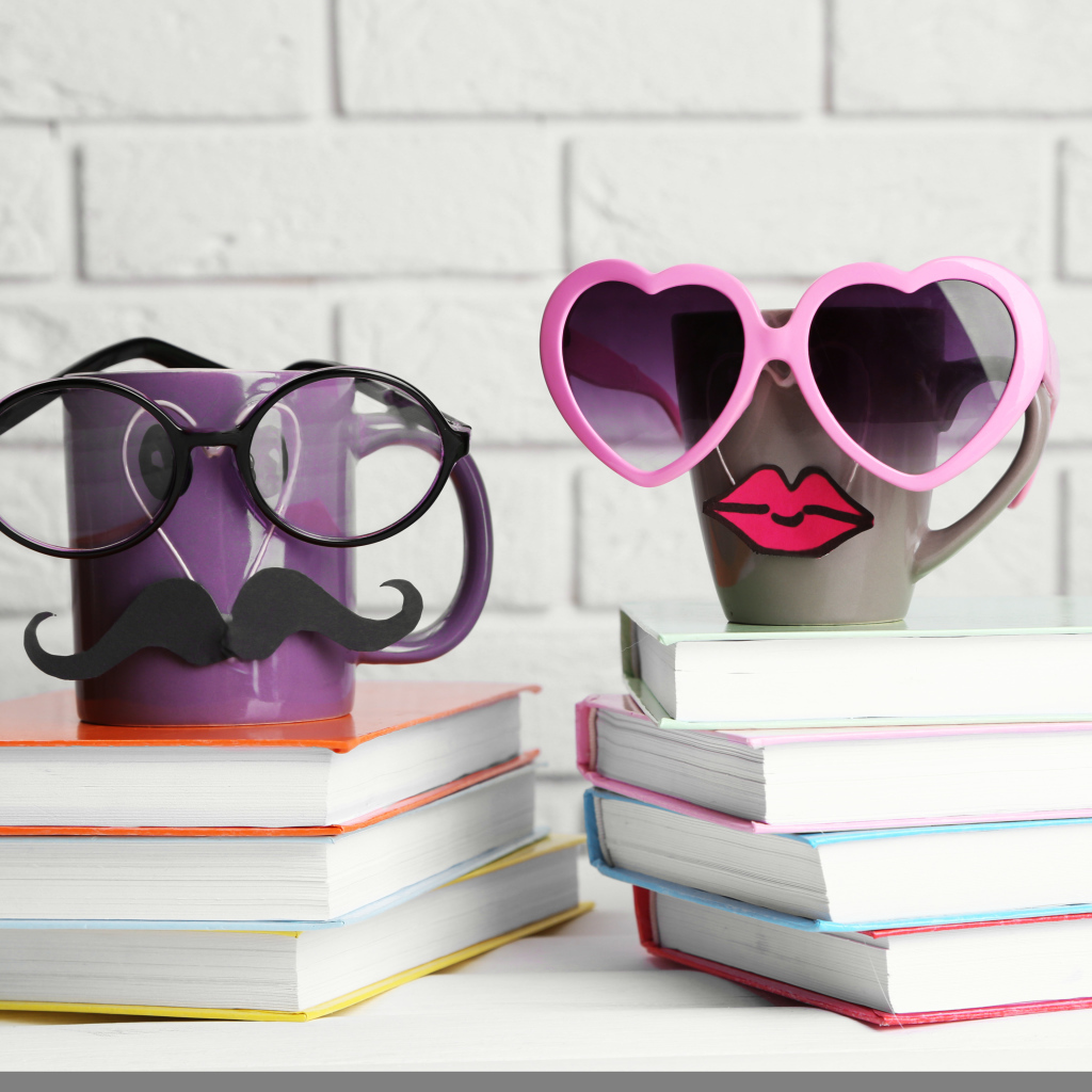Две забавные чашки в очках стоят на книгах