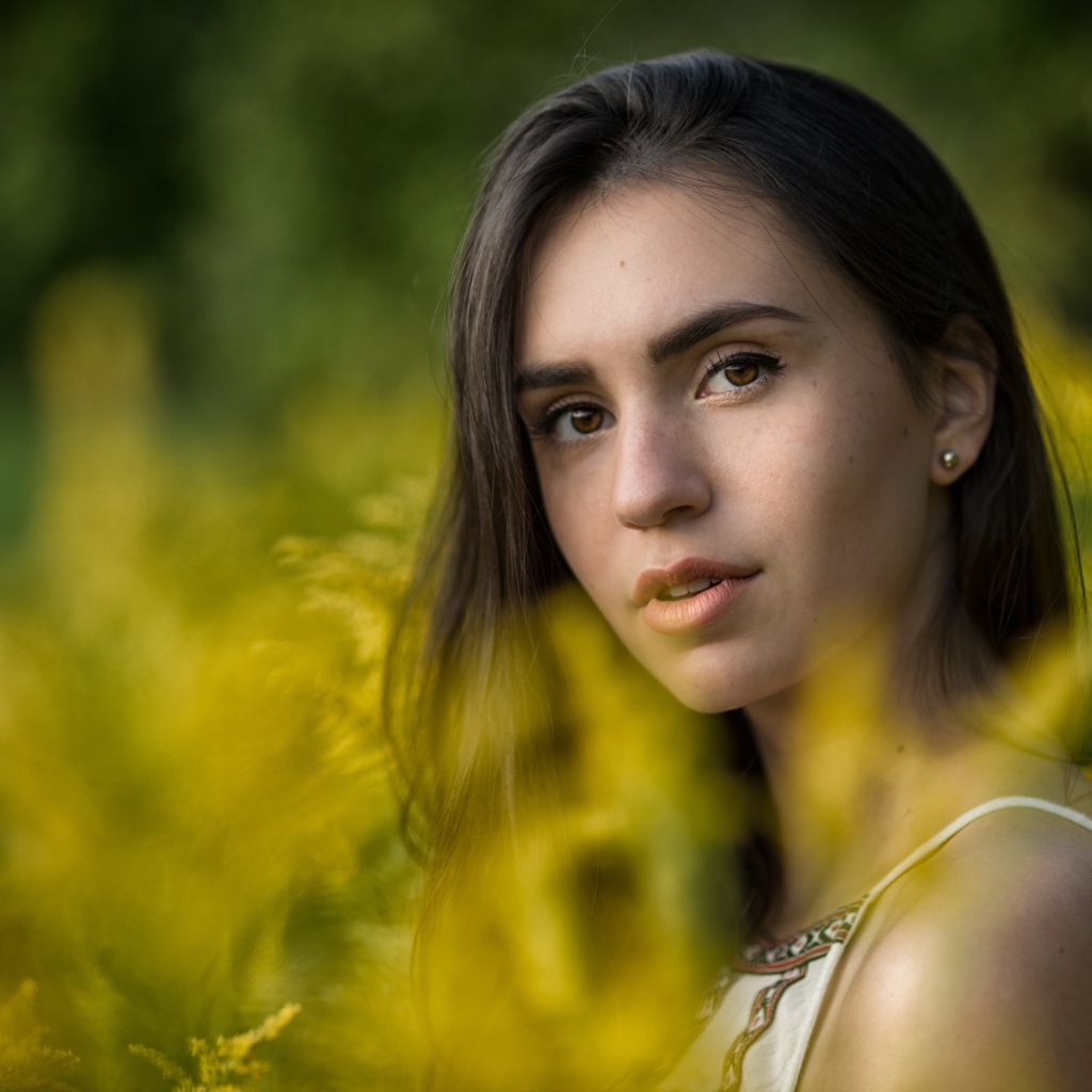 Красивая девушка с нежным взглядом сидит у желтых цветов