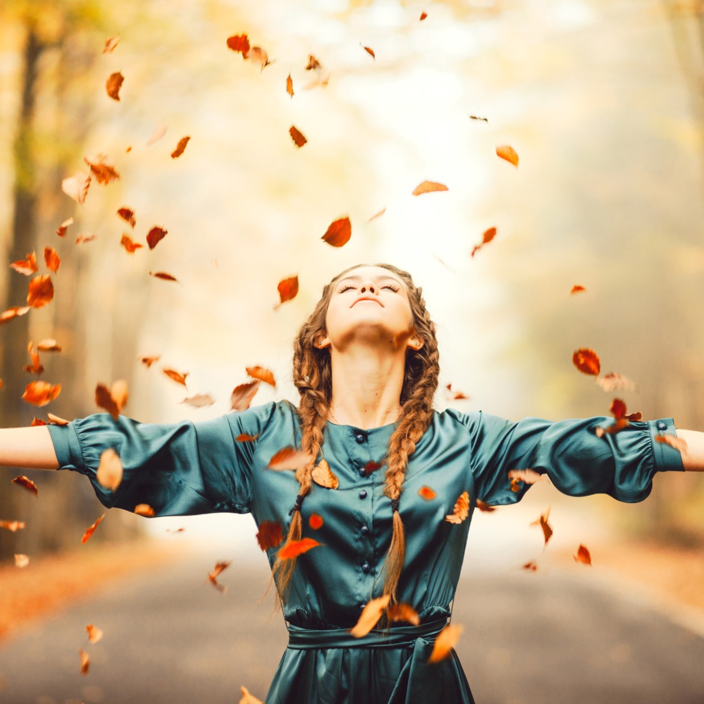 Красивая девушка с косичками подбрасывает желтые листья осенью