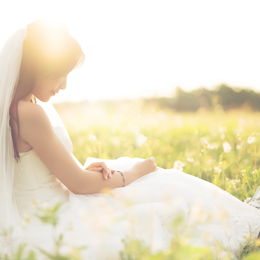 Девушка азиатка в платье невесты сидит на траве в поле 