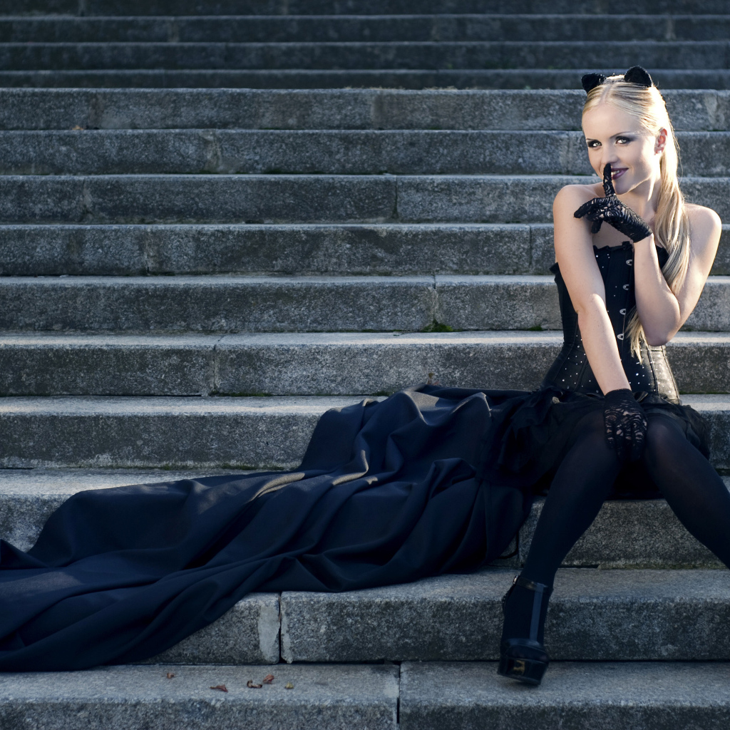 Красивая девушка блондинка  сидит на ступеньках в черном костюме