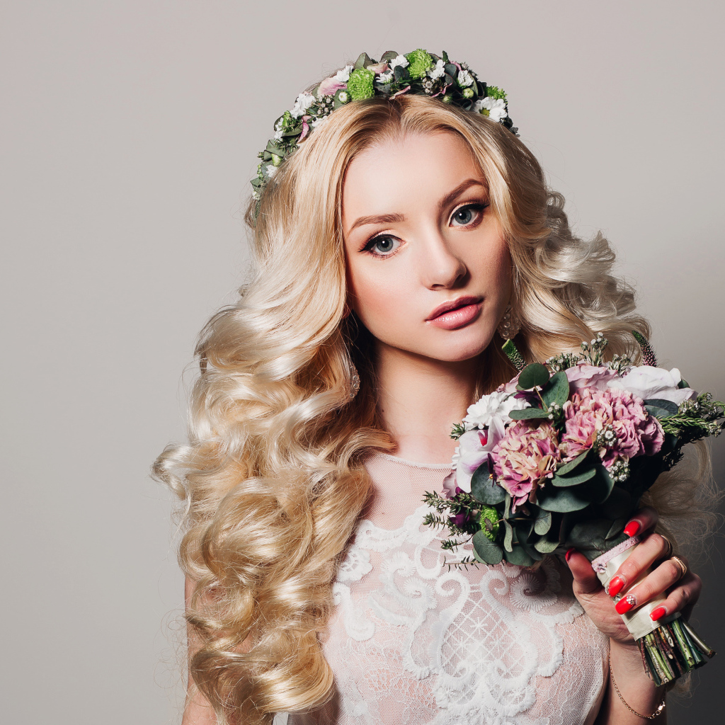 Красивая блондинка в свадебном платье с букетом цветов на сером фоне